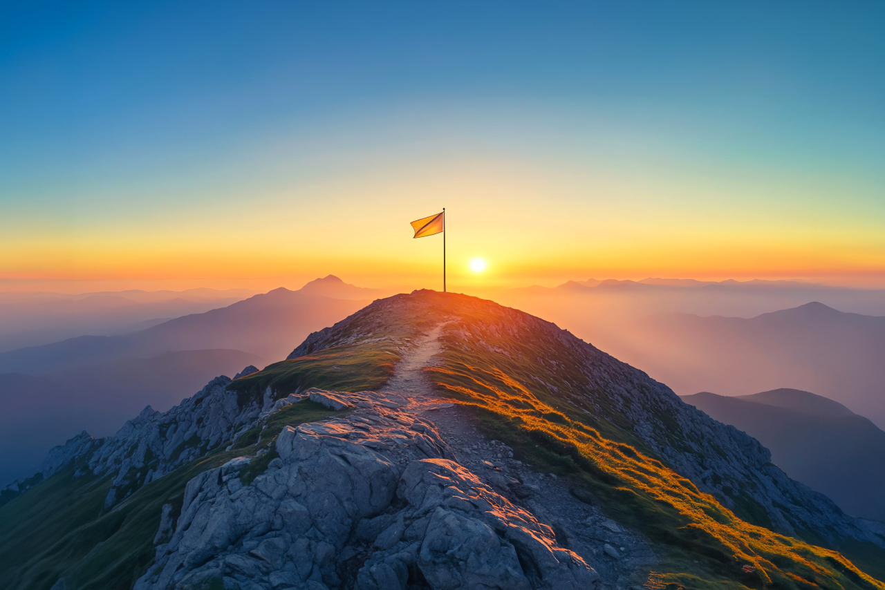 山頂に立つ旗と朝日の風景。人生の新たな目標やポジティブな変化を象徴するイメージ。